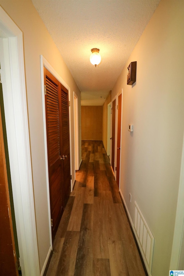 corridor featuring dark wood-style flooring, a textured ceiling, and visible vents