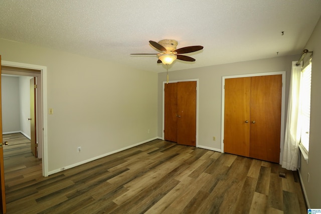 unfurnished bedroom with a textured ceiling, baseboards, multiple closets, and wood finished floors