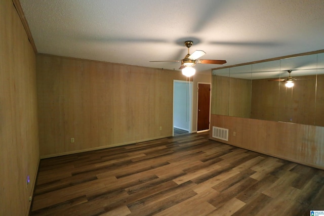 unfurnished room featuring visible vents, wood walls, wood finished floors, a textured ceiling, and a ceiling fan