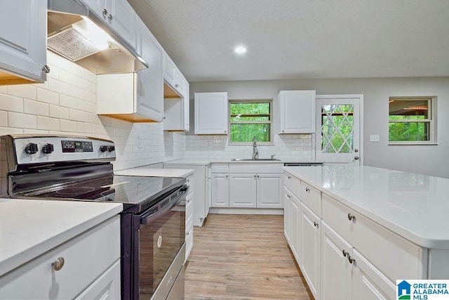 kitchen featuring under cabinet range hood, a sink, white cabinetry, stainless steel range with electric cooktop, and light wood-style floors