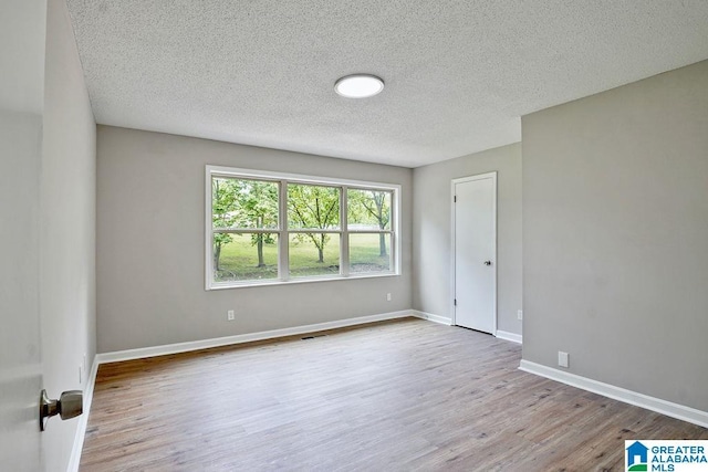 empty room with a textured ceiling, wood finished floors, and baseboards