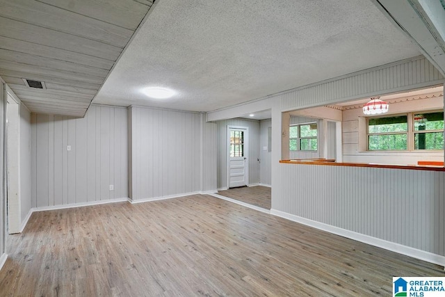 basement with a textured ceiling, baseboards, visible vents, and wood finished floors