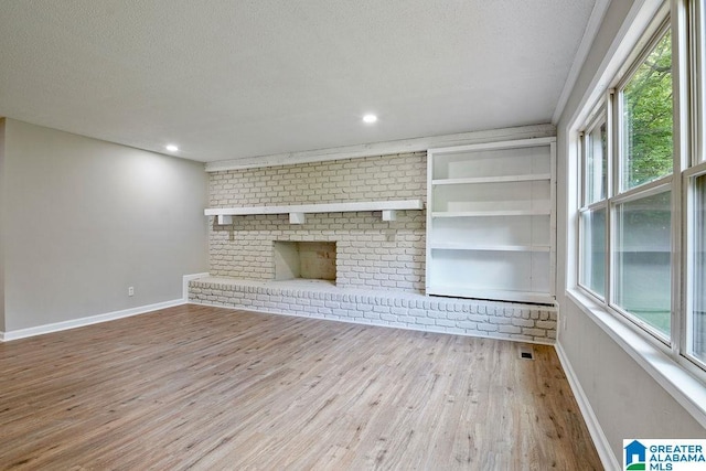 unfurnished living room with baseboards, a wealth of natural light, a textured ceiling, and wood finished floors