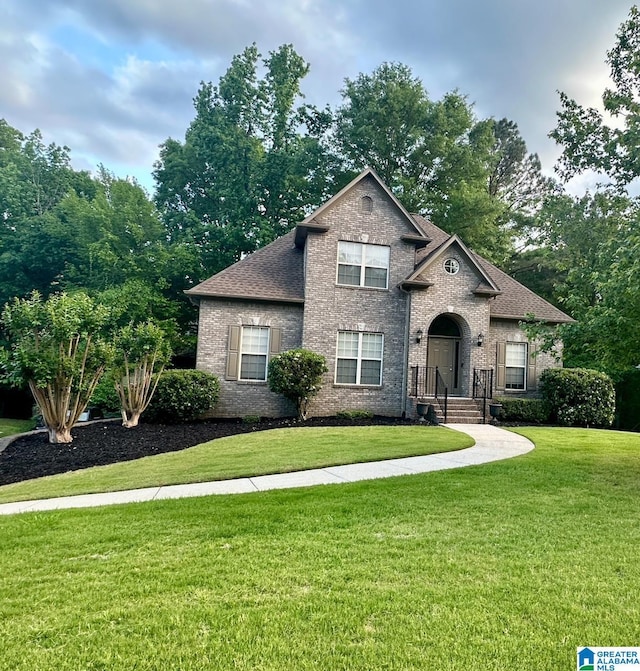 view of front of home featuring brick siding, a front yard, and a shingled roof
