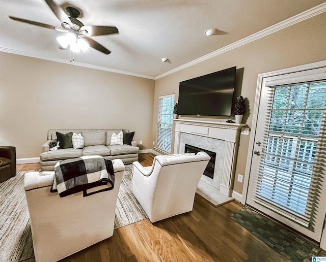 living area with dark wood finished floors, ornamental molding, a premium fireplace, baseboards, and a ceiling fan