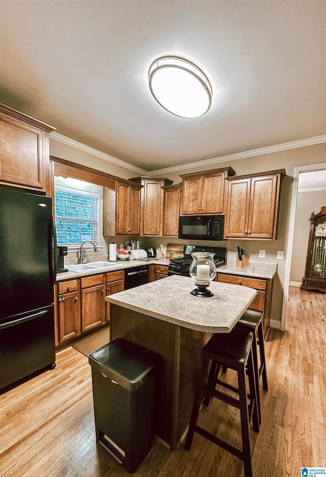 kitchen featuring black appliances, a sink, ornamental molding, a kitchen breakfast bar, and light countertops