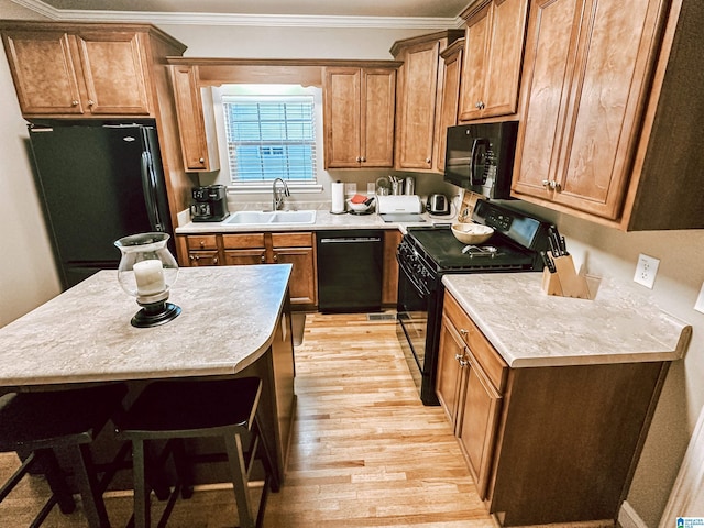 kitchen featuring black appliances, a sink, light wood-style floors, ornamental molding, and brown cabinets