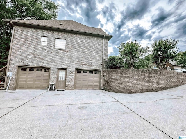 view of side of property featuring driveway, an attached garage, and brick siding