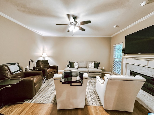 living area featuring a ceiling fan, wood finished floors, a fireplace, ornamental molding, and baseboards