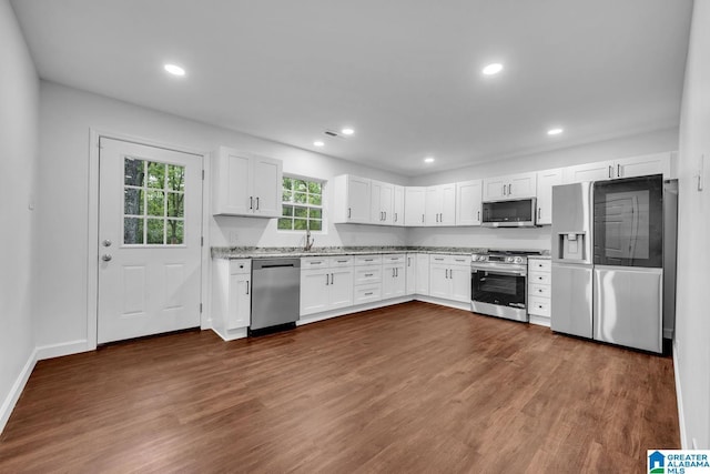 kitchen with dark wood-type flooring, white cabinetry, appliances with stainless steel finishes, and light stone counters