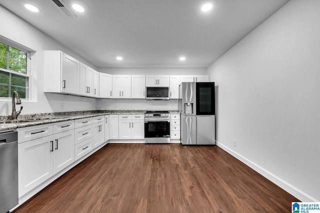kitchen with light stone countertops, a sink, dark wood finished floors, stainless steel appliances, and white cabinetry
