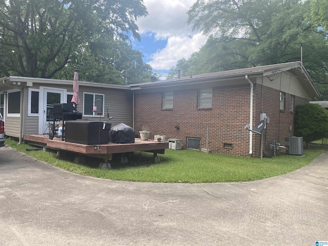 rear view of house with central AC, brick siding, a deck, crawl space, and a yard