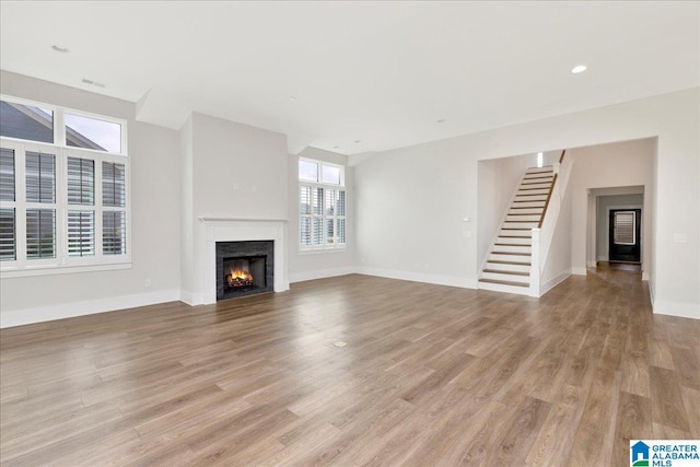 4546 Brexton St, Trussville, AL 35173 - unfurnished living room with a warm lit fireplace, baseboards, stairway, and light wood-type flooring