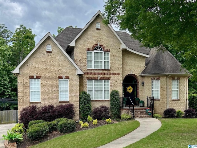 view of front of house featuring brick siding, a shingled roof, fence, and a front yard