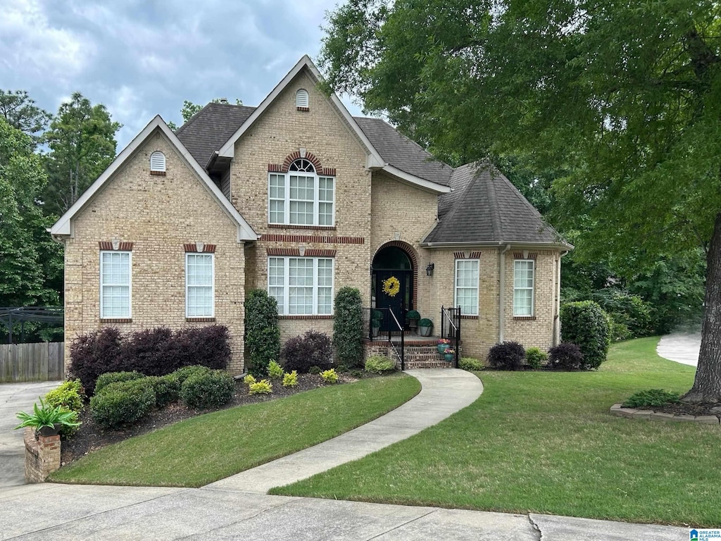 view of front of property featuring roof with shingles, fence, a front lawn, and brick siding
