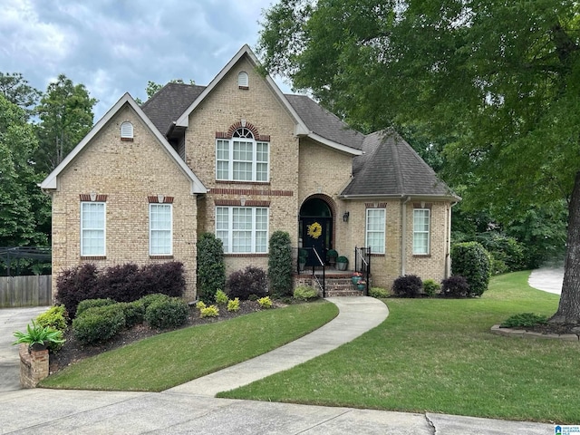view of front of property featuring roof with shingles, fence, a front lawn, and brick siding