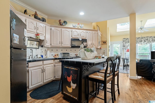 934 Chestnut Oaks Cir, Hoover, AL 35244 - kitchen with black appliances, tile countertops, a kitchen bar, ceiling fan, and a skylight