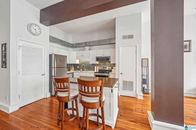 kitchen featuring appliances with stainless steel finishes, light wood-style floors, white cabinets, decorative backsplash, and a sink