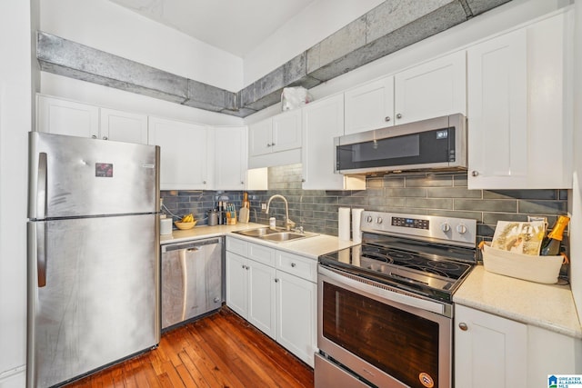 kitchen with appliances with stainless steel finishes, a sink, white cabinets, dark wood finished floors, and decorative backsplash