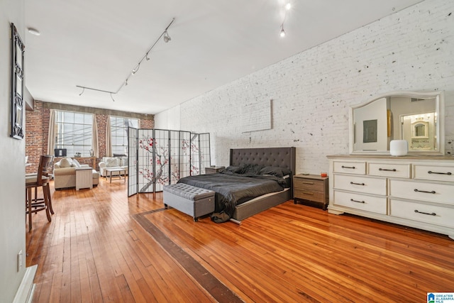 bedroom with brick wall, light wood-type flooring, and rail lighting