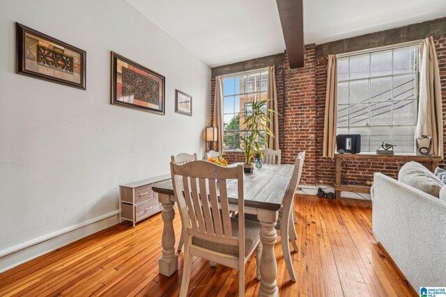 dining area with light wood-style flooring, baseboards, beamed ceiling, and brick wall