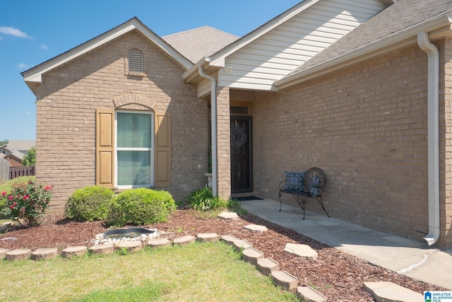 property entrance with a lawn, roof with shingles, and brick siding