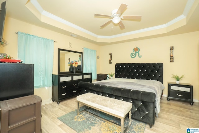 bedroom with a tray ceiling, crown molding, light wood-style floors, and visible vents