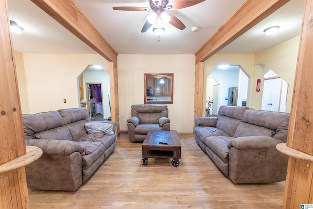 living area featuring a ceiling fan, light wood finished floors, and arched walkways