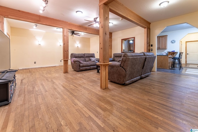 living room with ceiling fan, arched walkways, light wood-type flooring, and beam ceiling