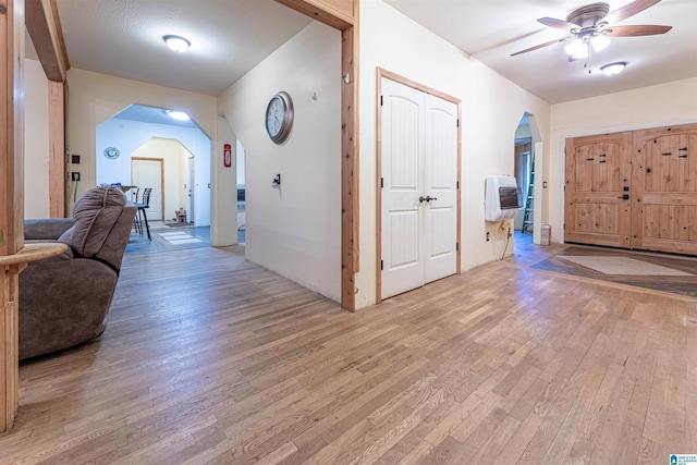 hallway with arched walkways, light wood-style floors, and heating unit