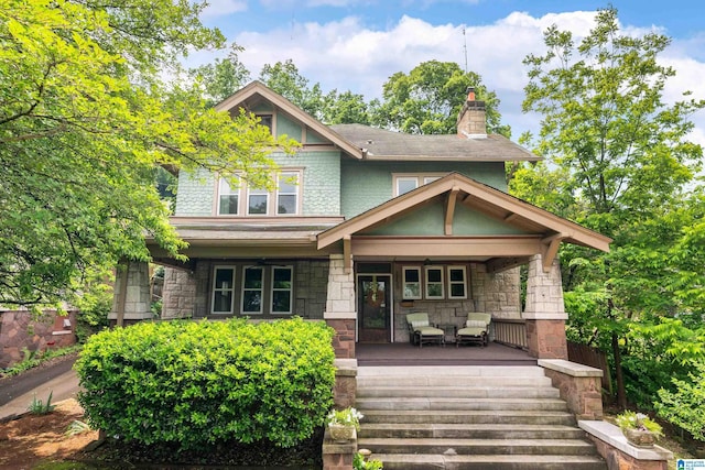view of front of home with a porch, stone siding, and a chimney