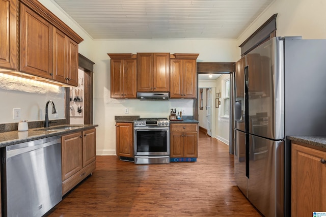 kitchen featuring stainless steel appliances, a sink, under cabinet range hood, dark wood-style flooring, and brown cabinets