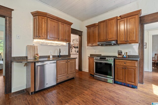 kitchen with stainless steel appliances, a sink, under cabinet range hood, and dark wood-type flooring