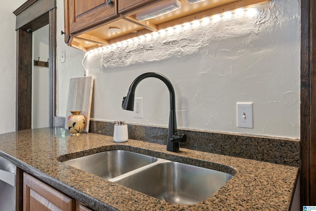 kitchen view of a sink, brown cabinetry, and dark stone counters