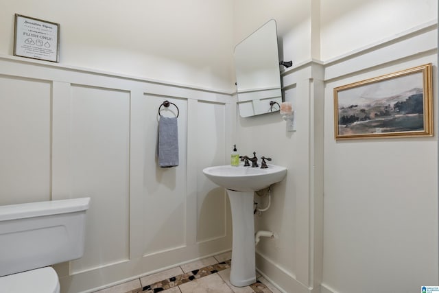 half bath with a decorative wall, tile patterned floors, toilet, a wainscoted wall, and inlaid floor details
