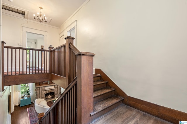 staircase featuring wood finished floors, a chandelier, and a fireplace