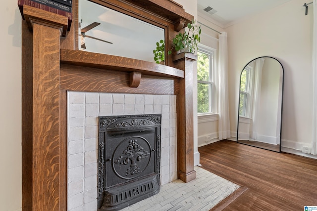 detailed view of a fireplace, wood finished floors, baseboards, a ceiling fan, and crown molding