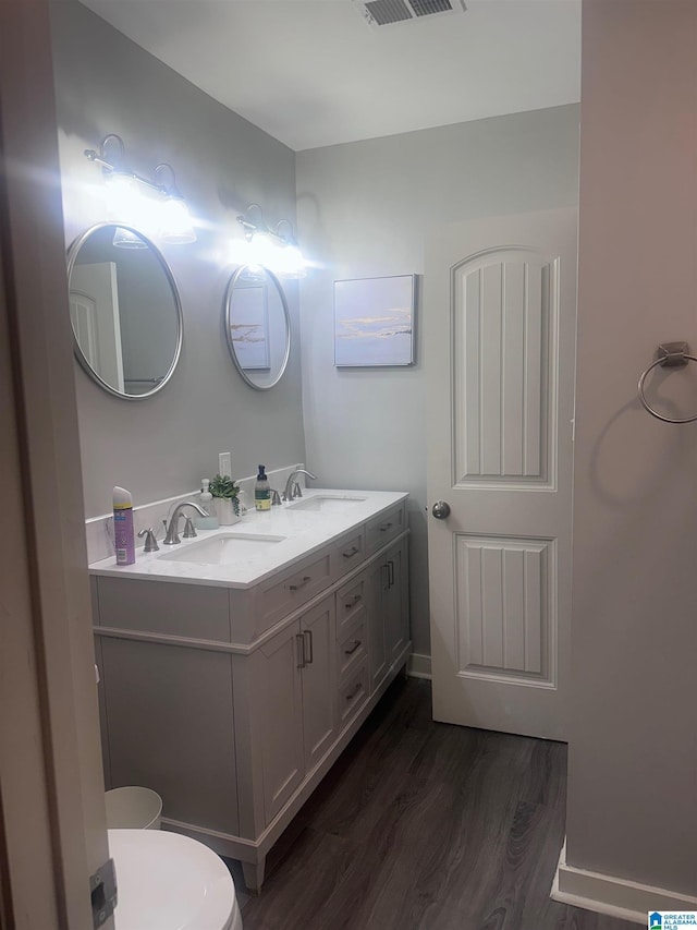 bathroom with double vanity, toilet, wood finished floors, a sink, and visible vents