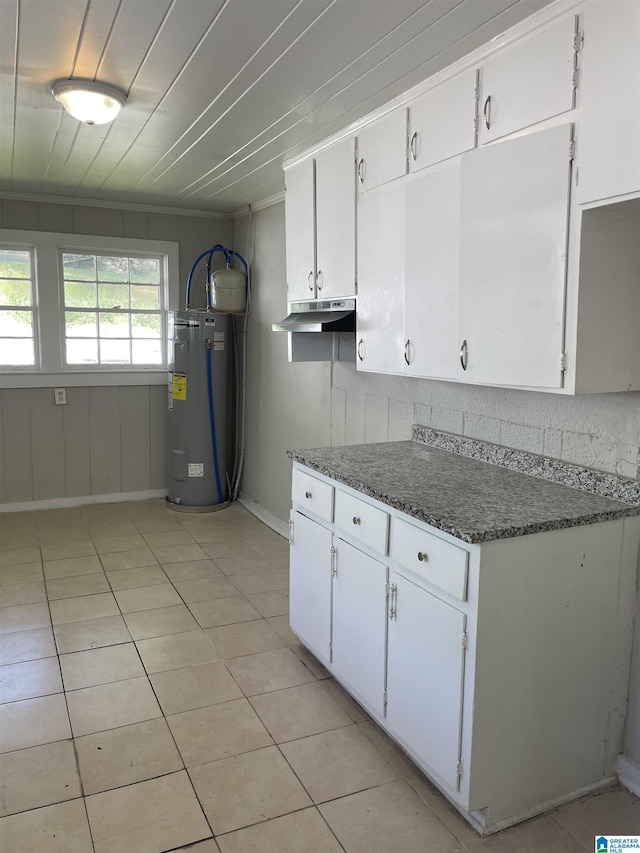 kitchen featuring light tile patterned floors, water heater, white cabinetry, baseboards, and under cabinet range hood