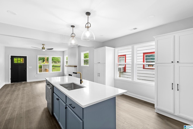 kitchen featuring a sink, wood finished floors, light countertops, stainless steel dishwasher, and baseboards