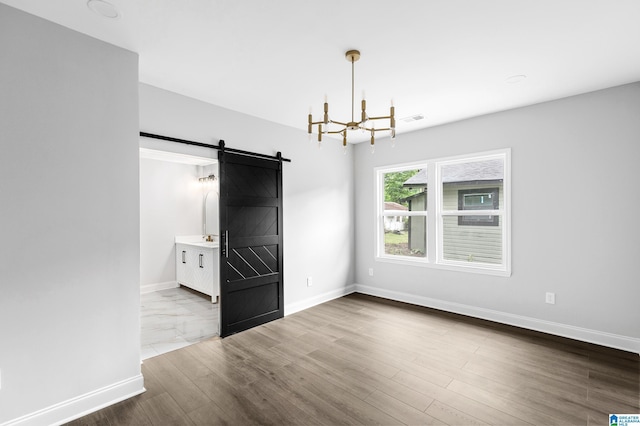 empty room with a barn door, a chandelier, baseboards, and wood finished floors