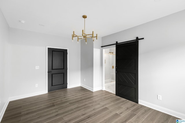 empty room with a barn door, a chandelier, dark wood-style flooring, and baseboards