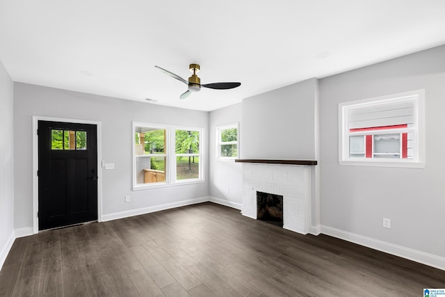 unfurnished living room with a ceiling fan, dark wood-type flooring, a brick fireplace, and baseboards