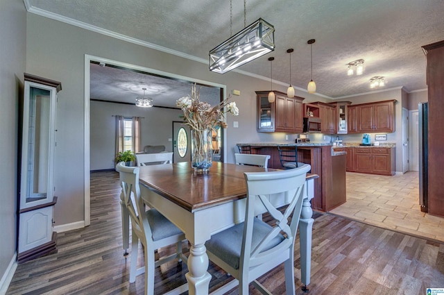 dining area featuring a textured ceiling, a chandelier, crown molding, light wood-style flooring, and baseboards