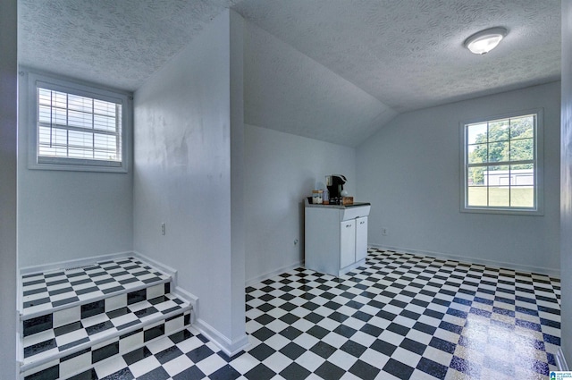 additional living space featuring baseboards, tile patterned floors, a textured ceiling, and vaulted ceiling