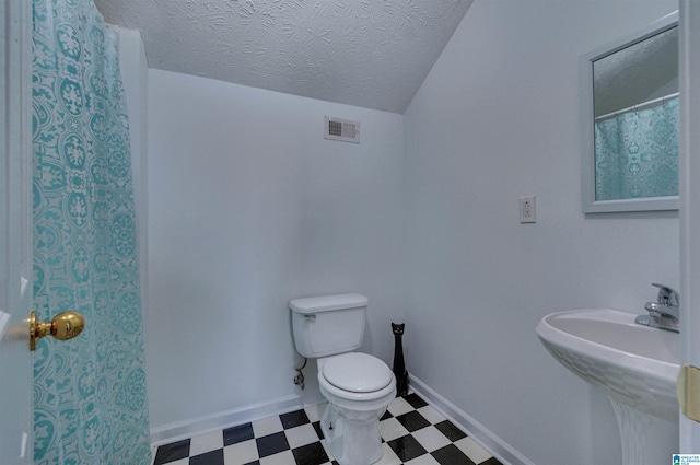 bathroom featuring toilet, a sink, tile patterned floors, a textured ceiling, and visible vents