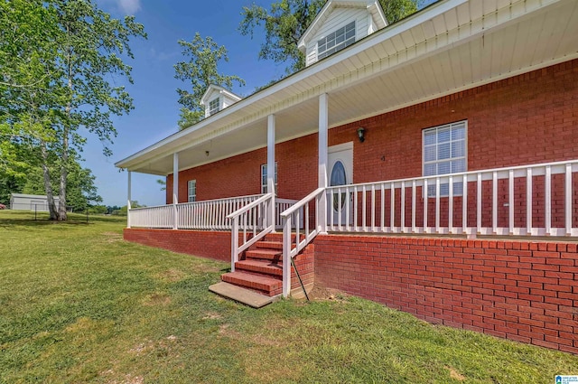 view of exterior entry featuring a yard, brick siding, and covered porch