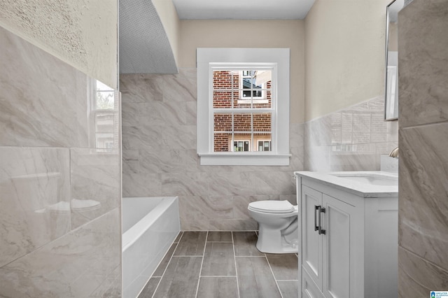1330 Bush Blvd W, Birmingham, AL 35208 - bathroom featuring tile walls, toilet, vanity, a bath, and a wainscoted wall