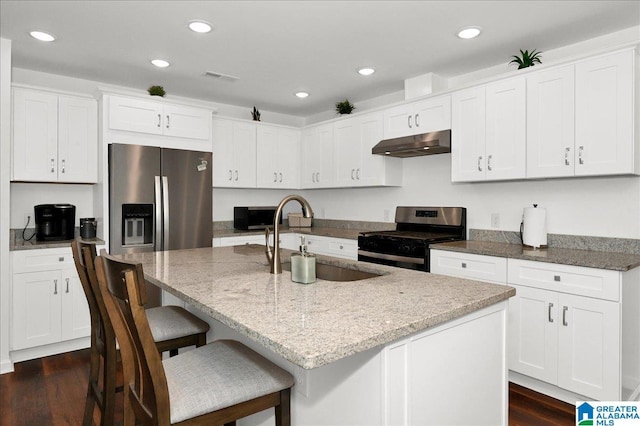 kitchen with a sink, stainless steel appliances, dark wood finished floors, under cabinet range hood, and light stone counters