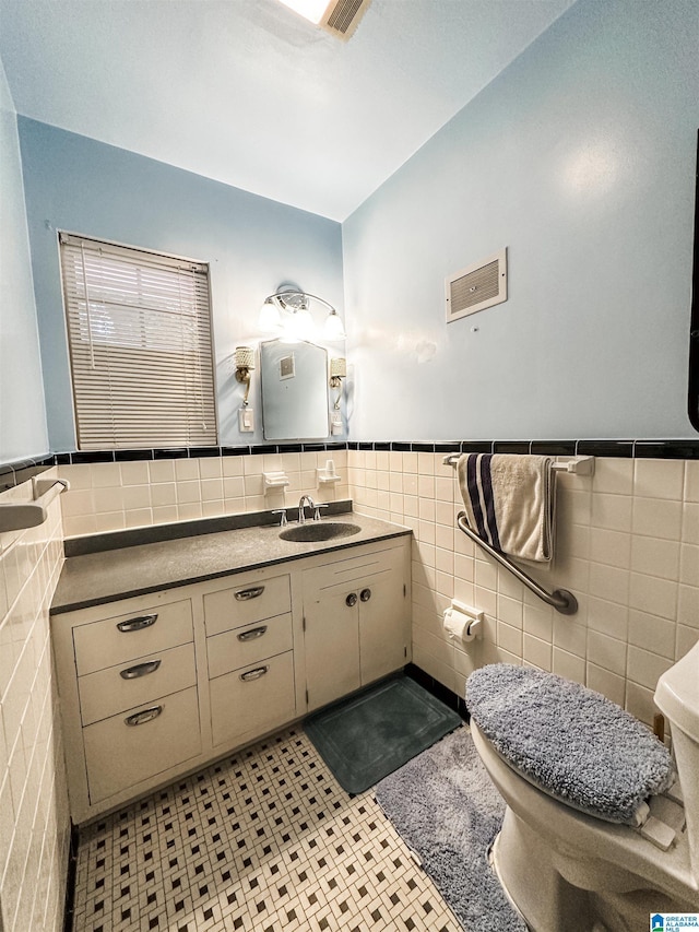 bathroom featuring tile walls, vanity, toilet, and wainscoting